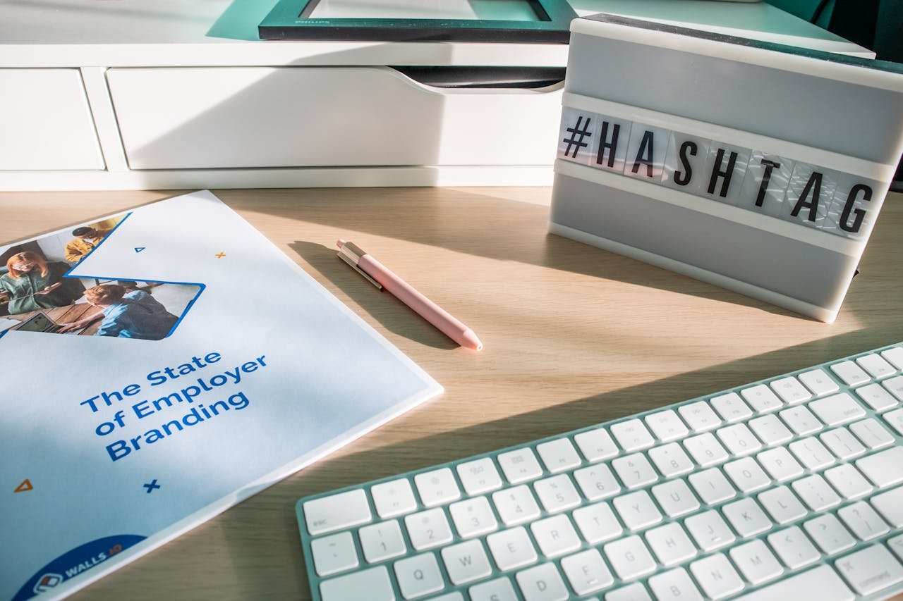 Bright workspace featuring an employer branding book, keyboard, and hashtag sign for tech-savvy branding purposes.